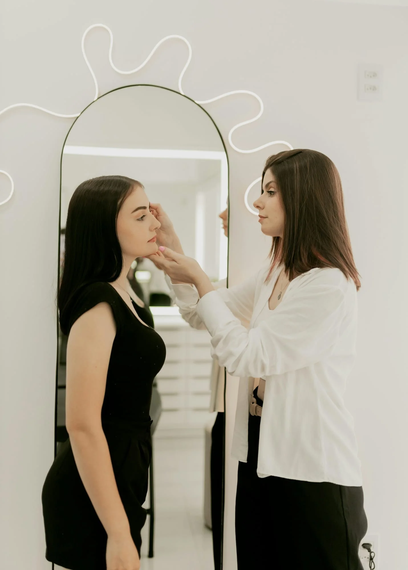 A practitioner looking at a client’s skin in front of a tall arched mirror.