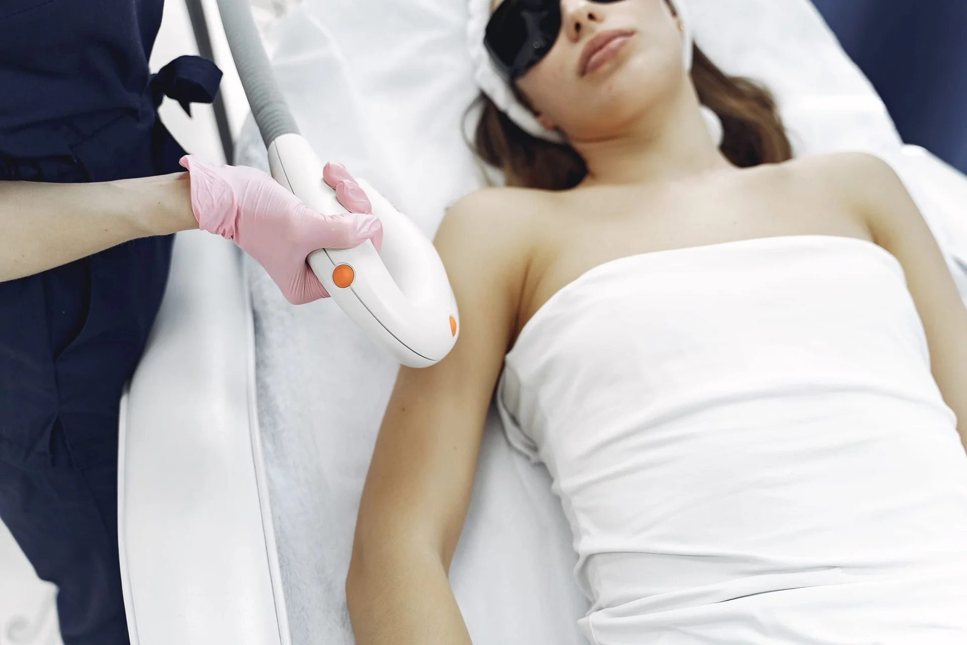 A laser hair-removal session: the client wears safety glasses on a white bed.