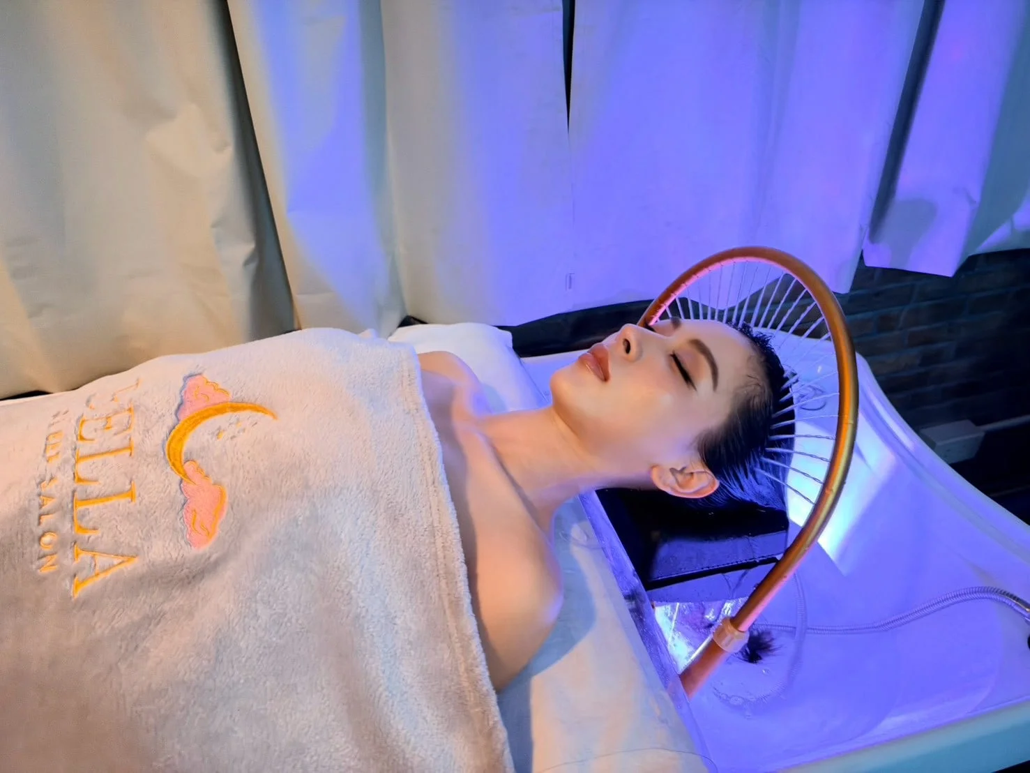 Ein Gast unter einem Handtuch des Bella Sleep Salon ruht unter dem Wasserbogen, in blauem Licht.