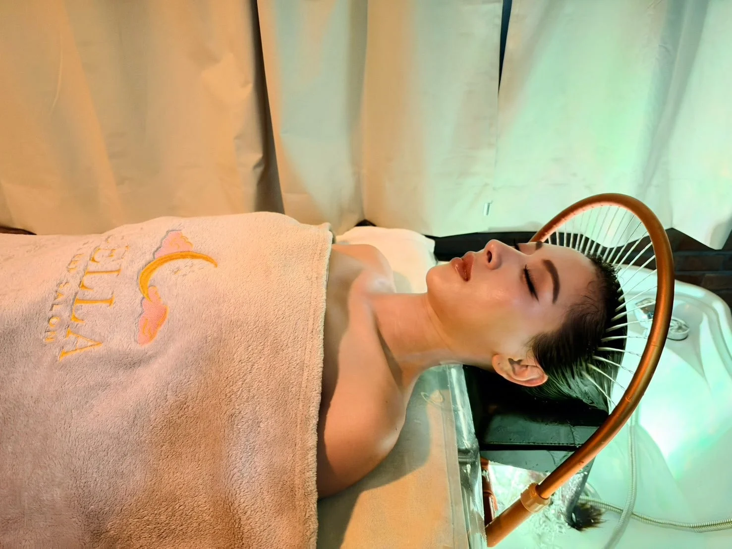 Ein Gast unter einem Handtuch des Bella Sleep Salon ruht unter dem Wasserbogen, in sanftem grünem Licht.