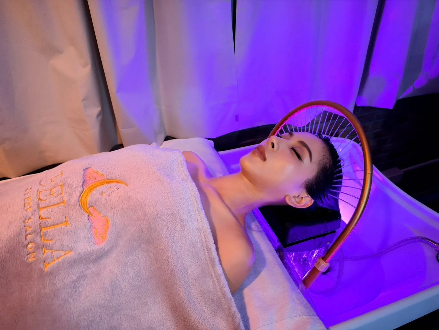 Ein Gast unter einem Handtuch des Bella Sleep Salon ruht unter dem Wasserbogen, in violettem Licht.