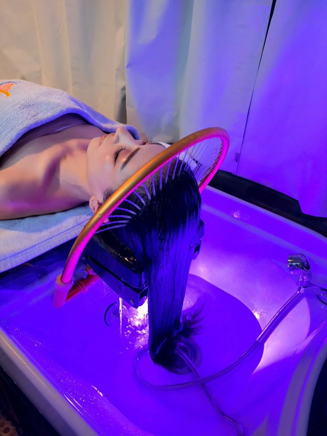 Haarwäsche unter dem geschwungenen Wasserbogen über dem Waschbecken, in violettem Licht.