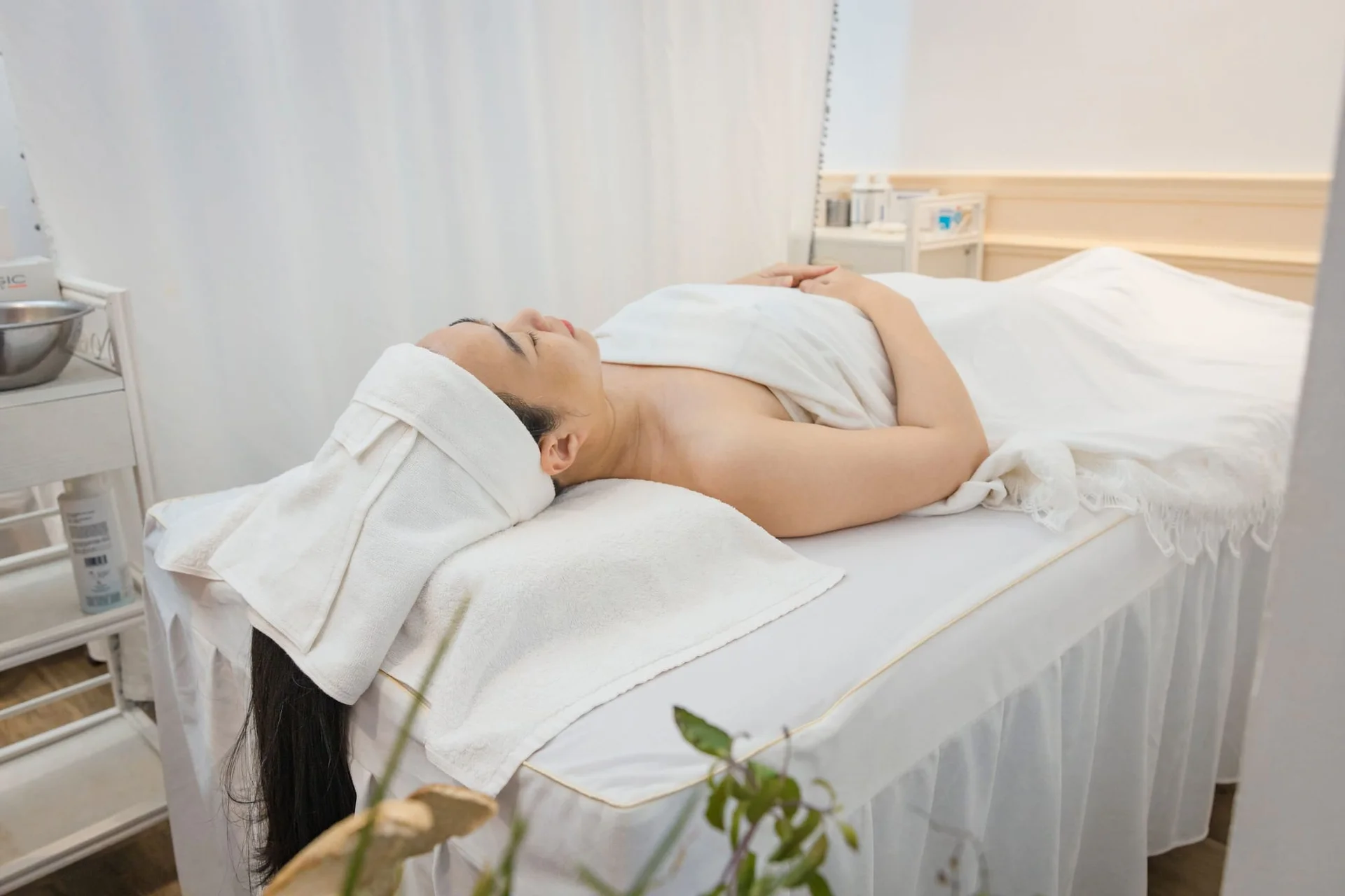 A client resting on a white-draped treatment bed after a facial.