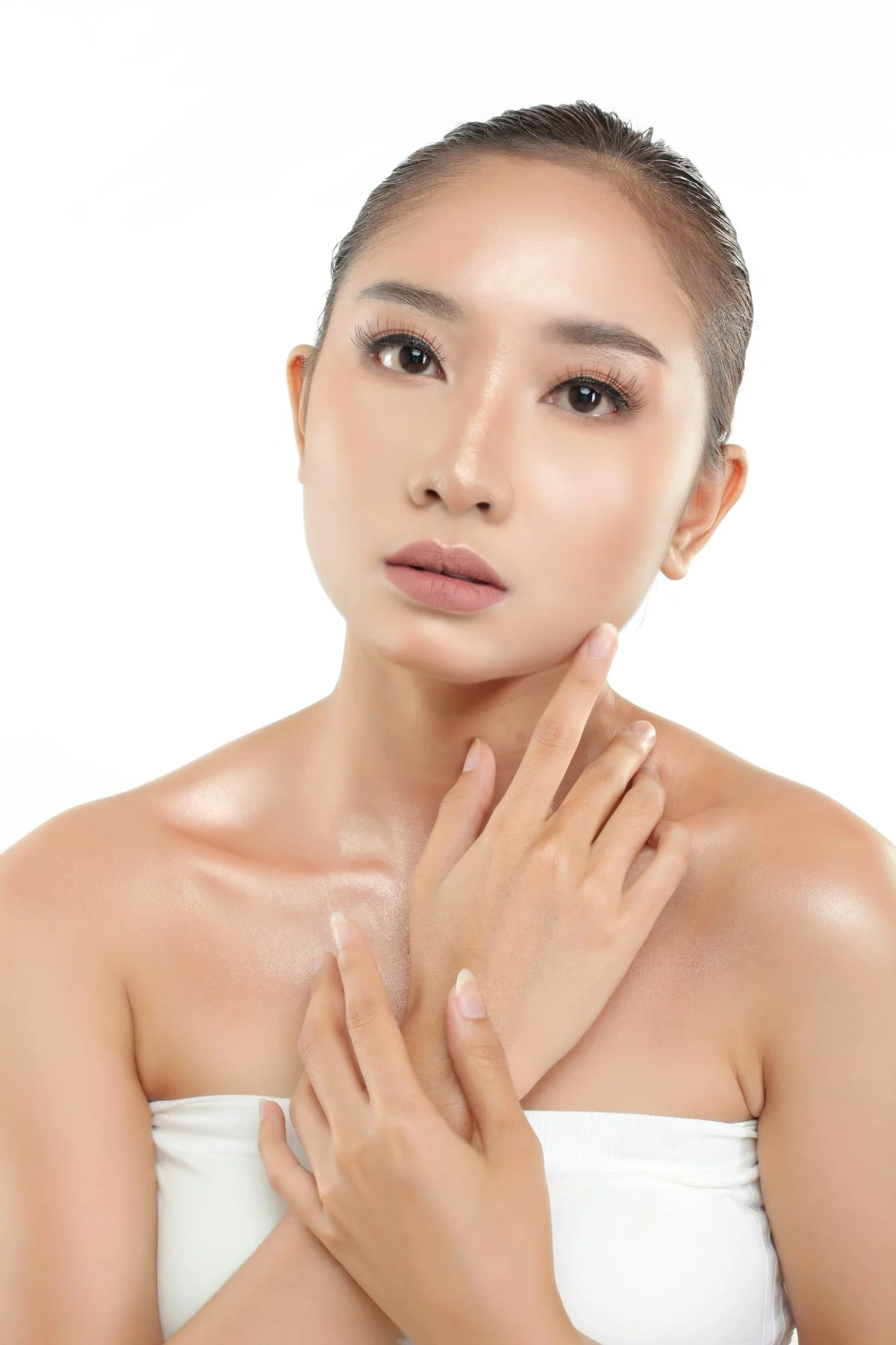 A calm portrait of a woman in white, hands at her collarbone, on a white background.