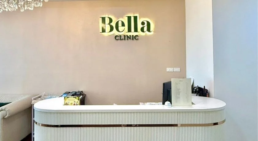The backlit Bella Clinic sign above the fluted white reception counter with its gold trim.