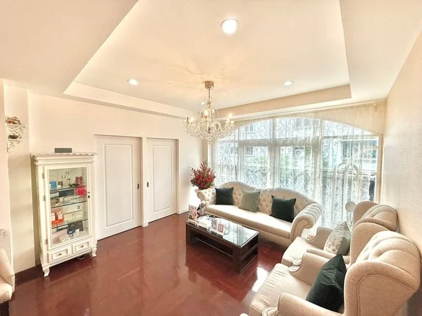 A bright sitting room with an arched lace-curtained window, cream sofas and a white display cabinet.